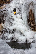 Ice climber climbing  frozen waterfall, Whorneyside Force, below Crinkle Crags, Lake District National Park, Cumbria, UK. February, 2021.