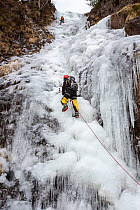 Ice climber on a frozen waterfall, Whorneyside Force, below Crinkle Crags, Lake District National Park, Cumbria, UK. February, 2021.