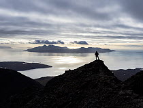 A mountain climber standing on the ridge enjoying the view from Sgurr Dearg on the Cuillin Ridge, towards the Isle of Rhum, Isle of Skye, Scotland, UK. October, 2021.