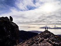 View looking past the Inaccessible Pinnacle, with two mountain climbers on the ridge, towards the Isle of Rhum, Isle of Skye, Scotland, UK. October, 2021.