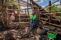Rosa Domingo sitting in house of her husband's other wife, Isabel Ofece Alfandega, damaged during Cyclone Idai. Outskirts of Gorongosa National Park, Mozambique. April 2019.