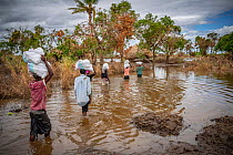 People wading through hip-deep water to bring emergency food parcels back home from distribution point, after Cyclone Idai. Outskirts of Gorongosa National Park, Mozambique. April 2019.