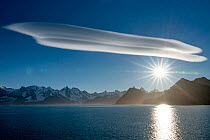 Lenticular clouds in a blue sky and bright sunlight over mountains, South Georgia Island, South Atlantic.