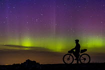 Mountain biker watching a display of aurora borealis lights across the night sky from the Cairngorm Plateau, Cairngorms National Park, Scotland, UK. September, 2015.