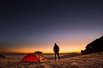 Man next to tent at a high camp on mountain ridge at sunset, Montana, USA. September, 2016.