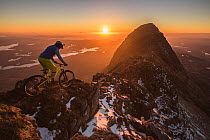 Mountain biker riding along mountain ridge at sunset, Suliven mountain, North West Highlands, Scotland, UK. March, 2017.