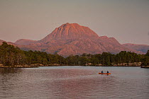 Canoeists on Loch Maree at dusk with a view of Slioch mountain in the background, Beinn Eighe National Nature Reserve, NW Highlands, Scotland, UK. September, 2020.