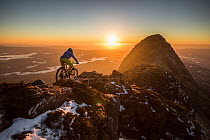 Mountain biker riding along mountain ridge at sunset, North West Highlands, Scotland, UK. May, 2017.