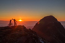 Mountain bikers high five after reaching the summit of Suilven at sunset, North West Highlands, Scotland, UK. May, 2017.