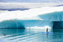 Woman paddling alongside curious Harbor seal (Phoca vitulina). Jokulsarlon Glacier Lagoon, Iceland. July.