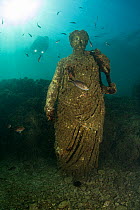 Scuba diver near ancient Roman Statue of Antonia minor, member of Julio-Claudian dynasty, daughter of Marcus Anthony and sister of emperor Augustus,  in submerged Nymphaeum of Emperor Claudius. Marine...