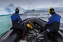 Two scuba divers on a boat returning  from a dive, Antarctic Peninsula, Antarctica, Southern Ocean.