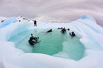 Scuba divers enjoying a swim in a pool of water formed in an iceberg, Antarctic Peninsula, Antarctica.