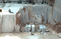 Man working in a  white marble quarry, surrounded by towering slabs of rock, Carrara, Tuscany, Italy. July.