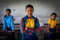 Portrait of Kusam Thanru, who received a scholarship to attend school from Nirajan Kshetria's honey business, alongside two girls in classroom, Bardia National Park, Terai, Nepal.