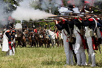 Cavalry standing on side while infantry fires guns, during First Empire military reenactment.  Montigny, Normandy, France. 2022.