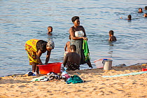 Local women washing clothes at lake banks, while children playing. Lake Malawi, Malawi.
