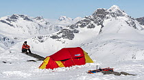 Photographer Orsolya Haarberg, sitting on snow next to her tent, camping on Mount Mugna, Jotunheimen National Park, Norway. April, 2021. Model released.