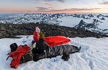 Two women camping overnight in bivy bag on the top of Mount Surtningssue, Jotunheimen National Park, Norway. June, 2021. Model released.