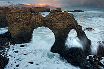 Natural arch rock formation over a surging storm tide, Arnarstapi, Snaefellsnes peninsula, Iceland. February.