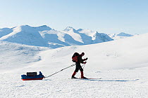 Man walking on skis and pulling sled on snow between Mount Kiertokiesjtjakka and Mount Nietter, with Mount Katoktjakka and Mount Piellorieppe the background, Sarek National Park, UNESCO World Heritage...