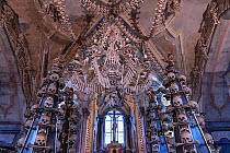An enormous chandelier of bones, which contains at least one of every bone in the human body, hanging from the center of the nave with garlands of skulls draping the vault in the Sedlec Ossuary, a sma...