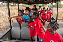 School children wildlife watching from open-sided bus, Gorongosa National Park, Mozambique. September, 2018.