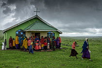 Local Maasai assistant Priest, Michael Chichilai, standing outside his church in the rain with his congregation after a Sunday service in Roman Catholic denomination church, Irkeepusi, Ngorongoro, Tan...