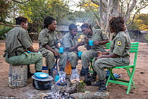 Five female park rangers, part of an all female ranger patrol, sitting together around a fire taking a break, Gorongosa National Park, Mozambique. June, 2018.