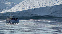 Tracking shot of a large iceberg and a tourist boat passing by, boat leaves frame, Ilulissat, Western Greenland, August, 2022.