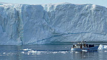 Tracking shot of a large iceberg and a tourist boat passing by, Ilulissat, Western Greenland, August, 2022.
