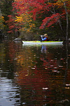 Woman kayaking on Grafton Lake and taking photographs in autumn, Enfield, New Hampshire, USA. October, 2021.