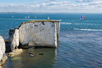 Old Harry's Rocks with people on jet skis and paddle boards nearby and a sailing regatta in the background, Studland, Dorset, English Channel, UK. July, 2022.