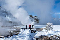 Tourists on viewing platform along the Firehole River in winter, surrounded by frost-covered trees and snow, Biscuit Basin, Yellowstone National Park, Wyoming, USA. January, 2022.