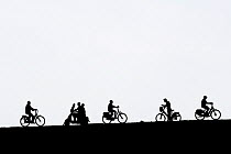 Motor scooter riding past cyclists and man on bicycle checking his smartphone silhouetted against white background, Netherlands. Digitally enhanced silhouette.