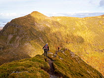 Two hikers walking along ridgeline in Quinag mountains, Assynt, Scotland, UK. October, 2022.