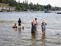 Asian women and children paddling in Lake Windermere, cooling off during the July 2022 heatwave, Lake Windermere, Lake District, Cumbria, UK. July, 2022.