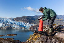 Photographer sorting out equipment during fieldwork in Tempano Fjord, with glacier in background. Bernardo O'Higgins National Park, Patagonia, Chile. February.