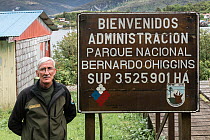 Ranger coordinator of Bernardo O'Higgins National Park standing in front of welcome sign in Puerto Eden village.  Bernardo O'Higgins National Park, Patagonia, Chile, February.