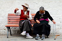 Two women sitting on bench sewing with coloured wool on Barkhor kora, pilgrimage circuit in old centre of Lhasa.  Lhasa, Tibet, China.