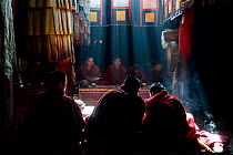 Monks during prayer ceremony shrouded in rays of light and incense smoke.  Shelkar Chode Monastery (at 4,300m), Tibet, China.