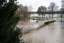 People crossing Victoria Bridge with high water levels on the River Wye, surrounded by floodwater across the King George V playing fields, Herefordshire, England, UK. 14th January 2023.