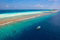 Aerial view of Dhigurah Island with a traditional Maldivian Dhoni boat at the reef edge, South Ari Atoll, Maldives, Indian Ocean. February, 2020.