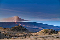 Pair of cinder cones from an old eruption sprout vegetation on the slopes of Mauna Kea Volcano as Mauna Loa Volcano erupts with lava spilling down its northern slopes, Big Island, Hawaii, USA. Decembe...