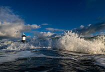 Crashing waves with Penmon lighthouse in background, near Beaumaris, Anglesey, Gwynedd, Wales, UK. December. 2022.