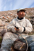 Inuk man holding Little auk (Alle alle) caught with net, to prepare for kiviak, Siorapaluk, Greenland.