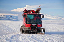 Pisten Bully vehicle transporting filmmakers from Ross Island over the sea ice, with active volcano Mount Erebus behind, Antarctica, Ross Sea.