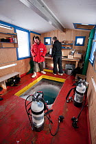 Two divers inside dive hut, preparing to dive under thick sea ice, McMurdo Sound, Ross Sea, Antarctica.