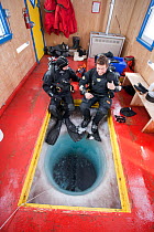 Two divers inside dive hut, preparing to dive under thick sea ice, McMurdo Sound, Ross Sea, Antarctica.