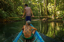 Village chief Apai Bandi traveling up Utik River with Dayak boatman on canoe, Sungai Utik Customary Forest, Kalimantan, Borneo, Indonesia.